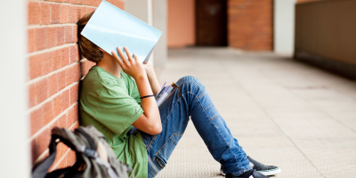 Vermoeid schoolkind verbergt gezicht met een boek