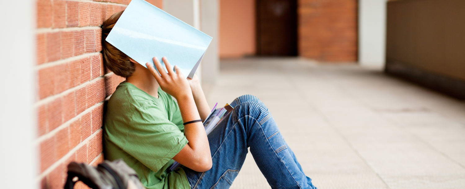 Vermoeid schoolkind verbergt gezicht met een boek